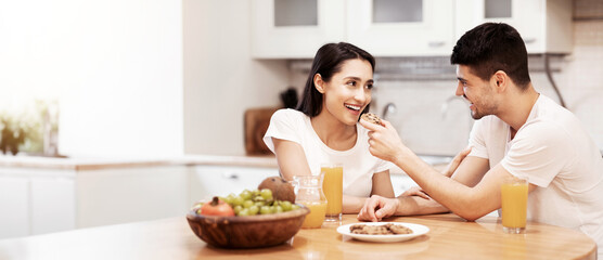Happy Loving Family Concept. Smiling guy feeding his girl with cookies, couple having breakfast...