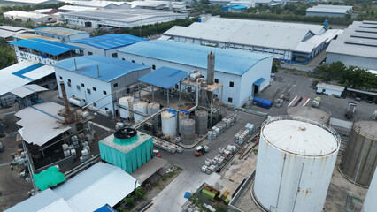 A busy factory with large tanks and trucks loading and unloading. The industrial activity is constant, with vehicles moving between towering storage units.