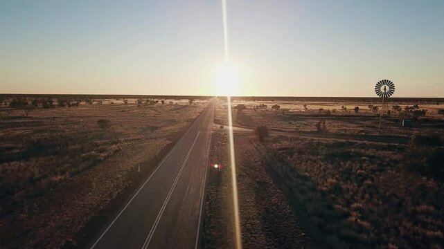 Aerial view. Silhouette of a large windmill in central Australia rotating in slow motion against dramatic Australian outback sunset. No people. Red center Uluru