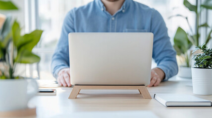 detailed view of ergonomic laptop stand with employee working at desk, showcasing modern workspace with plants and stationery. setup promotes comfort and productivity