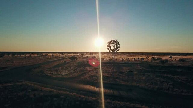 Aerial view. Silhouette of a large windmill in central Australia rotating in slow motion against dramatic Australian outback sunset. No people. Red center Uluru