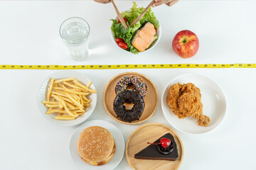 Woman choose healthy food for diet. Healthy food and fatty food separated on table with measuring tape. Lose weight, balance, control, reduce fat, low calorie, routine, exercise, body shape..