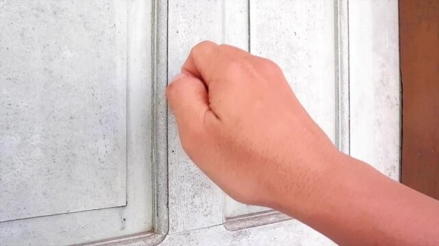 A Man's Hand Was Knocking For Quite A Long Time On A Weathered White Door, With Sunlight Shining On Its Surface
