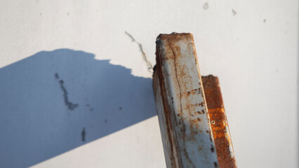 Rusty metal plate with shadow on white wall. Shallow depth of field.