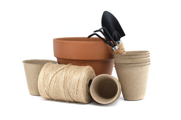 Gardening tools with terracotta pot, biodegradable pots, and spool of twine on a white background