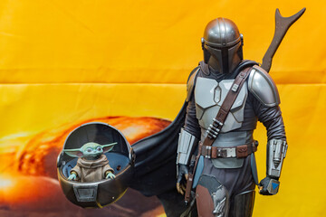 Naklejka premium 8th Comic Con Convention In GUAYAQUIL, ECUADOR - AUG 06, 2023 -Mandalorian and Grogu figurines against vibrant orange background, inspired by the Star Wars series. Perfect for sci-fi and collectible