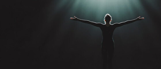 Obraz premium A silhouette of a person with outstretched arms against a dark backdrop, symbolizing freedom and self-expression under beams of light.