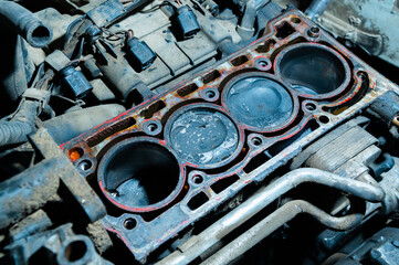 An exposed disassembled internal combustion engine. The engine block contains dirty pistons with carbon deposits and broken pieces of metal. The concept of lack of car care and untimely engine service