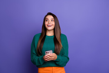 Fototapeta premium Photo of nice young girl hold phone look empty space wear pullover isolated on purple color background