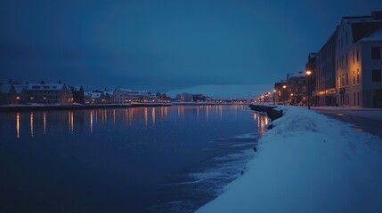 Naklejka premium Scenic view of Reykjavik city center during the blue hour, with twinkling lights reflecting off the water and snow-covered streets. No people included.