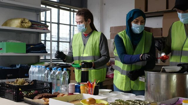 Group of multiracial volunteers in a uniform helping people at charity center. Humanitarian aid concept. Muslim woman and her colleagues working in homeless shelter. Diversity.