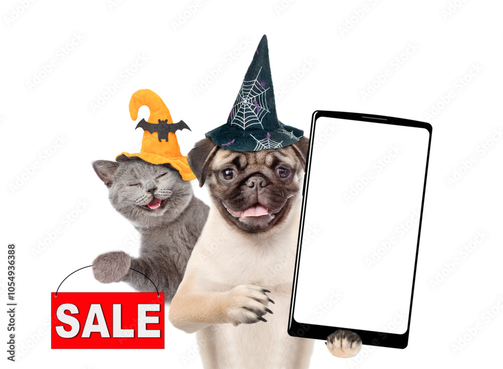 Poster happy cat and pug puppy wearing hats for halloween looks at camera. dog shows smartphone with white 