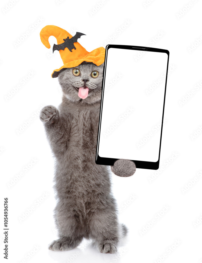 Fototapete surprised cat wearing hat for halloween holds shows smartphone with white blank screen in it paw. is