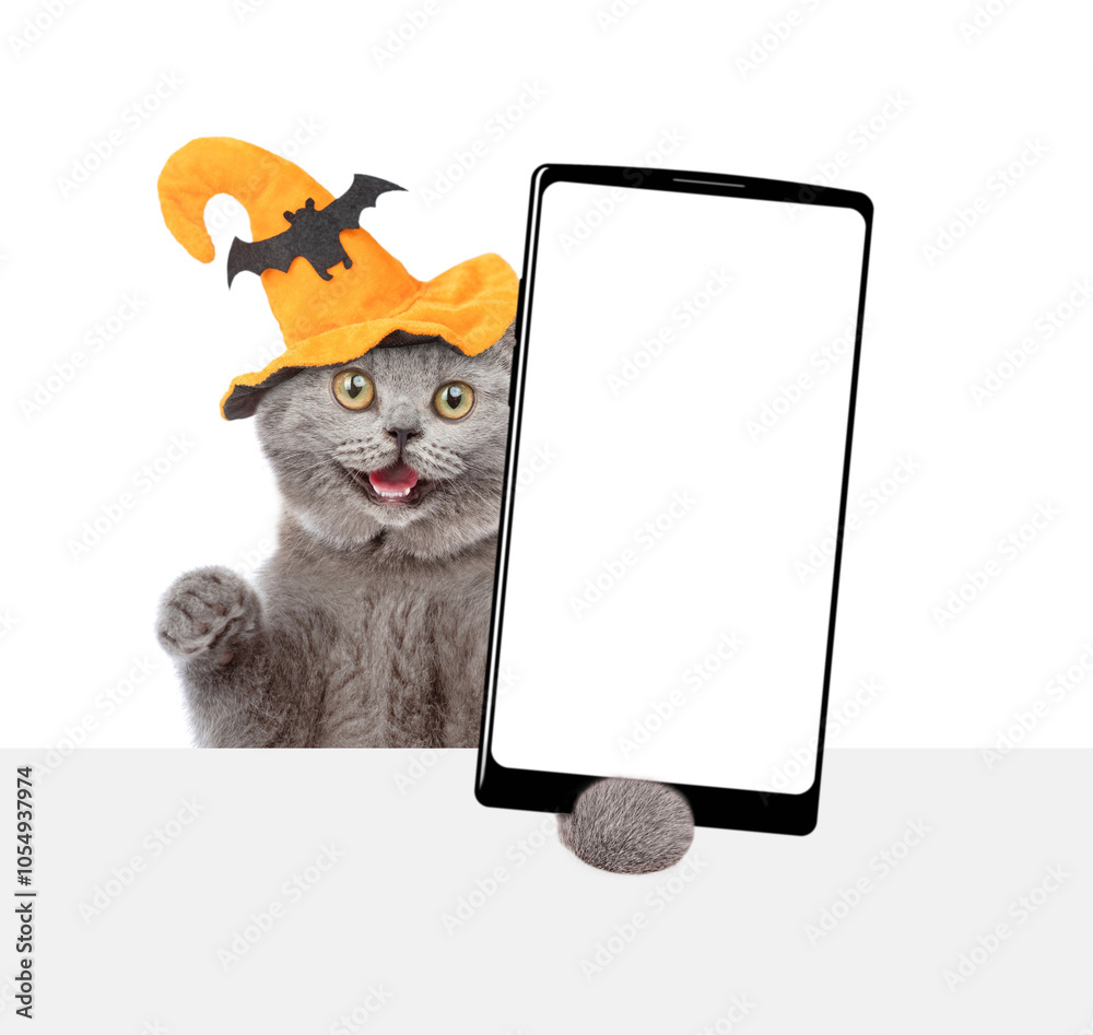Poster surprised kitten wearing hat for halloween holds shows smartphone with white blank screen in it paw 
