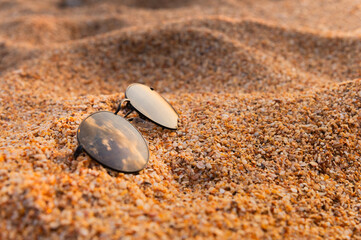 sunglasses lying on the beach on wet sandy sand. close up of stylish accessory during vacation, nobody