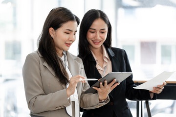 Professional female colleagues employees looking at digital tablet tech discussing corporate project at work.