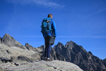 Male hiker with backpack enjoying breathtaking view of mountain peaks on clear sunny day