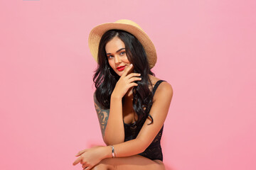 Summer studio shot portrait of beautiful Caucasian woman wearing swimming suit and sun hat posing in pink color isolated background