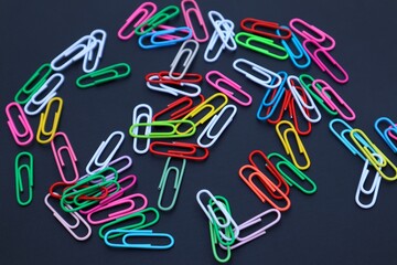 Colorful elliptical paper clips scattered on a dark background, close-up view.