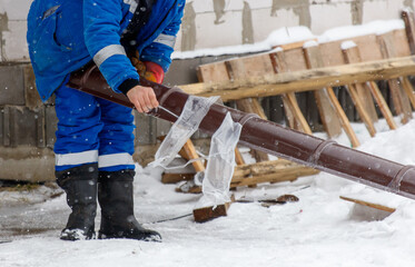 A man in a blue coat is working on a pipe in the snow
