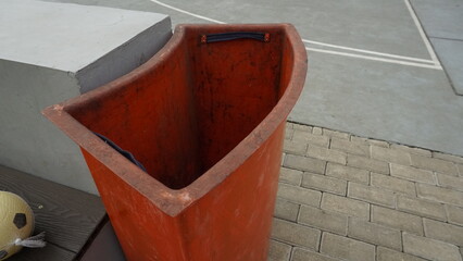 An orange trash can on the edge of a park
