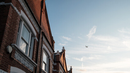 Airplane flying over typical english terraced houses in london suburb at sunset