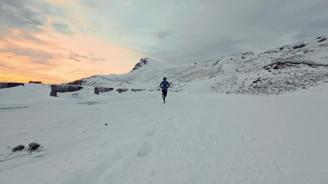 Aerial drone view of young man jogging outdoors with snowy mountains in the background. Healthy running and exercise concept outdoors, high-speed drone fvp shooting, slow motion