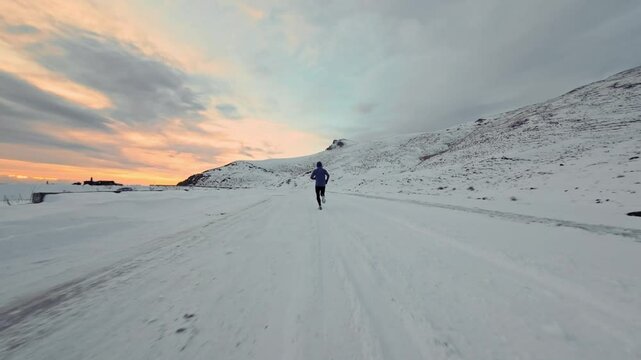 Aerial drone view of young man jogging outdoors with snowy mountains in the background. Healthy running and exercise concept outdoors, high-speed drone fvp shooting, slow motion