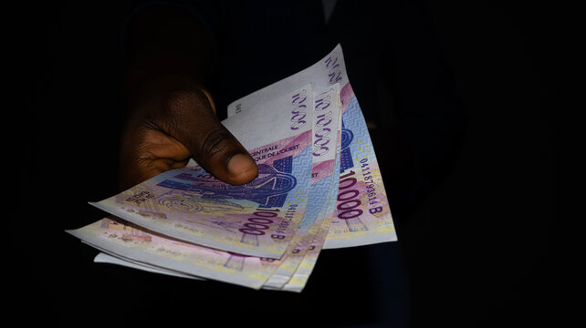 Black female  hand holding West African cfa franc notes over dark background, currency of west africa
