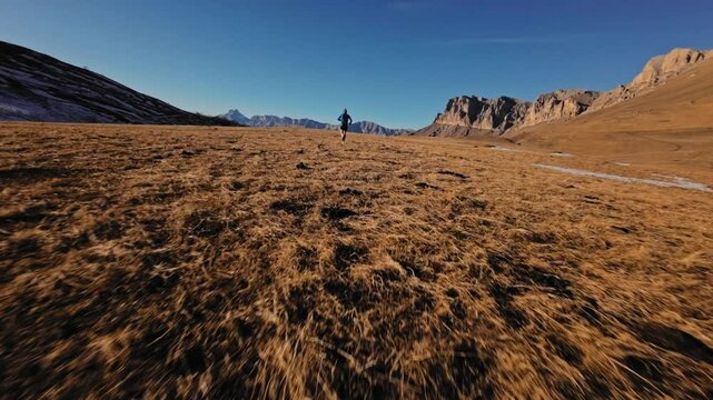 Aerial view of a man in sportswear running fast across fields. A guy exercising outdoors in nature in the mountains covered with snow. View from below near the legs, healthy lifestyle
