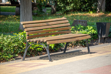 A wooden bench sits on a sidewalk in a park