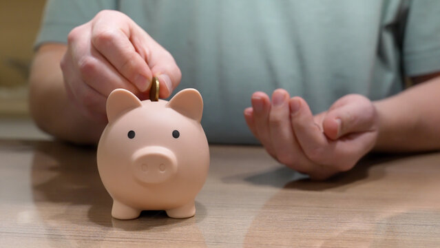 A person is adding a coin to a piggy bank while managing their finances to prepare for retirement. This highlights the importance of saving and budgeting over time. Money Savings Concept.