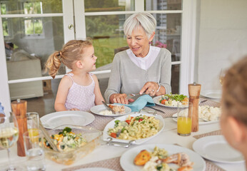 Grandmother, lunch and happy child eating food at patio table for thanksgiving celebration at home. Generations, kids and share meal with girl at family gathering on holiday for nutrition or health