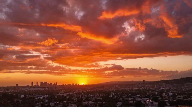 Dramatic orange clouds in beautiful fiery sunset sky over Los Angeles cityscape and West Hollywood / Century City skyline. Aerial hyperlapse timelapse view.