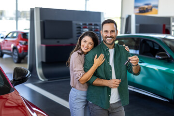 Visiting car dealership. Beautiful couple is holding a key of their new car, looking at camera and smiling