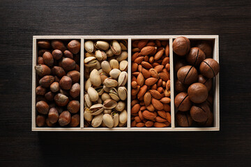 Fototapeta premium Wooden box with different nuts on a dark background