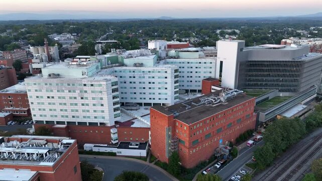 Aerial orbit shot of UVA Health University Hospital in Charlottesville City. Early morning in american town along tracks of train. Green Trees and mountains during fall season. Wide shot.