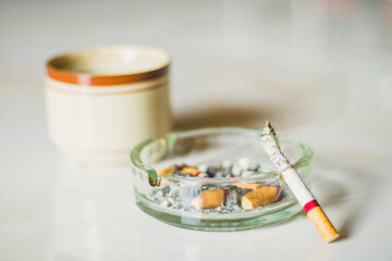 A cigarette with long ashes in the ashtray with a cup of drink