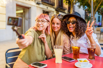 Women gesturing success while taking selfie with camera at bar