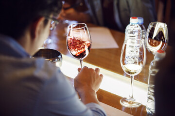 Sommelier Tasting Glass of Red Wine, Swirling it Sitting at Table