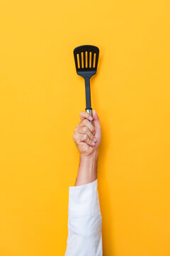 Chef hand holding spatular and raising in yellow isolated background, cooking equipment concept