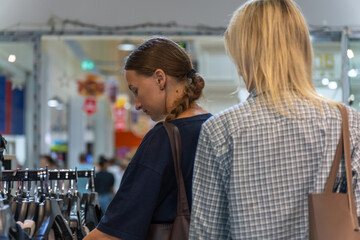 Two young women shopping for clothes, choosing from a variety of shirts in a stylish store, immersed in the world of fashion and consumerism