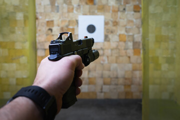 Shooting a pistol with a red dot sight at a paper sport target at a shooting range.