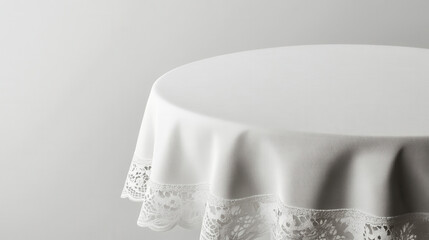 A plain white tablecloth drapes elegantly over a round table, featuring delicate lace detailing along the edge against a minimal background.