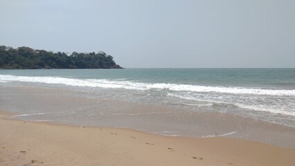 Serene beach scene with gentle waves and forested hill.