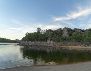 Reservoir surrounded by mountains and green vegetation with clouds reflecting on the water at sunset