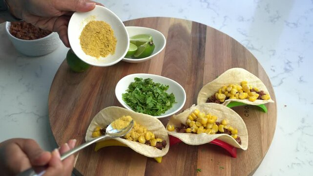 Tacos filled with fresh ingredients, kitchen counter top down view, spiced powder mix sprinkled onto open soft shells