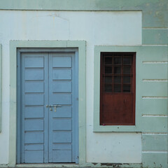 Blue door with pale green color concrete wall and wooden window with brown colored and dark glasses