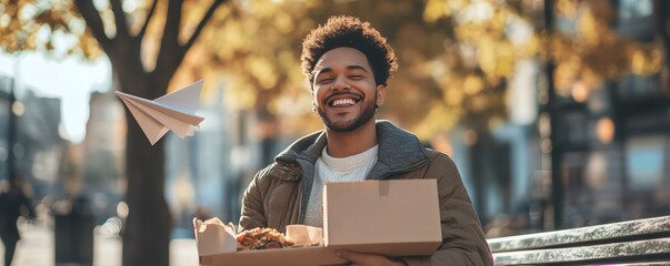 Smiling man, coffee, playful paper plane, food box, park bench