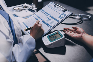 A doctor taking a patient's blood pressure. The patient's arm is equipped with a blood pressure...